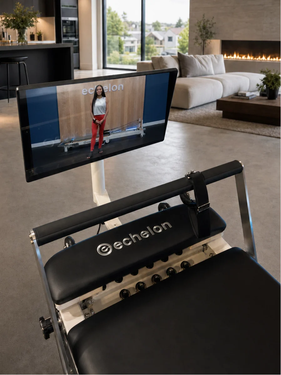 An Echelon Pilates reformer with an attached screen shows an instructor in a modern living room.