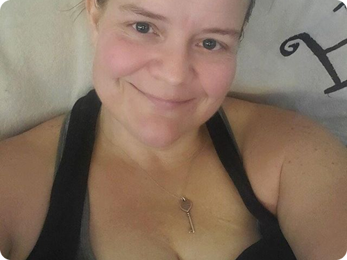 A person smiling, wearing a black top and a necklace with a key pendant.