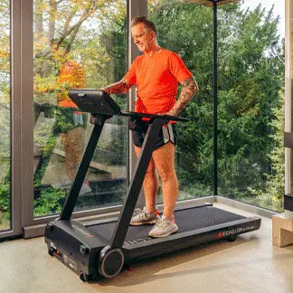 Person using a treadmill indoors with large windows and forest view.
