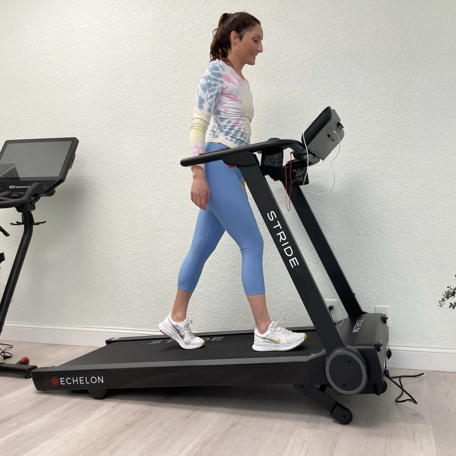 A woman walking on a treadmill indoors near an exercise bike.