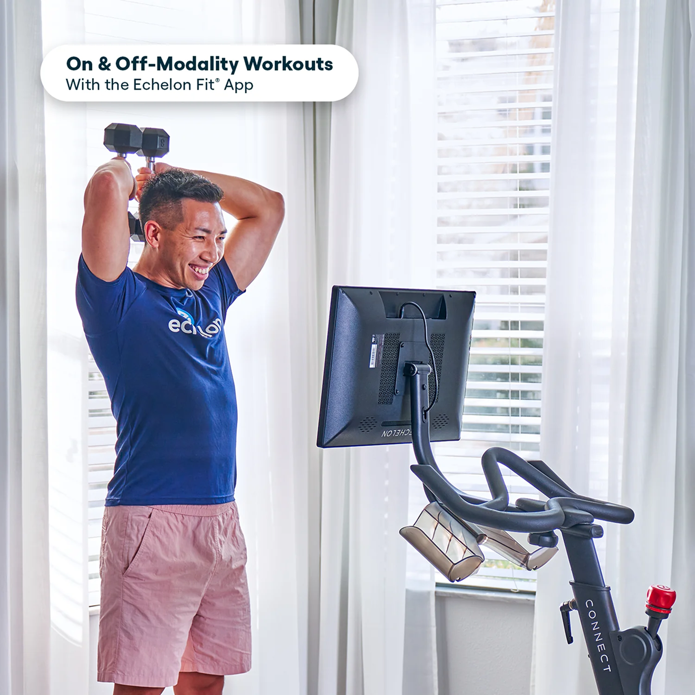 Person exercising with dumbbells near a monitor and stationary bike indoors.