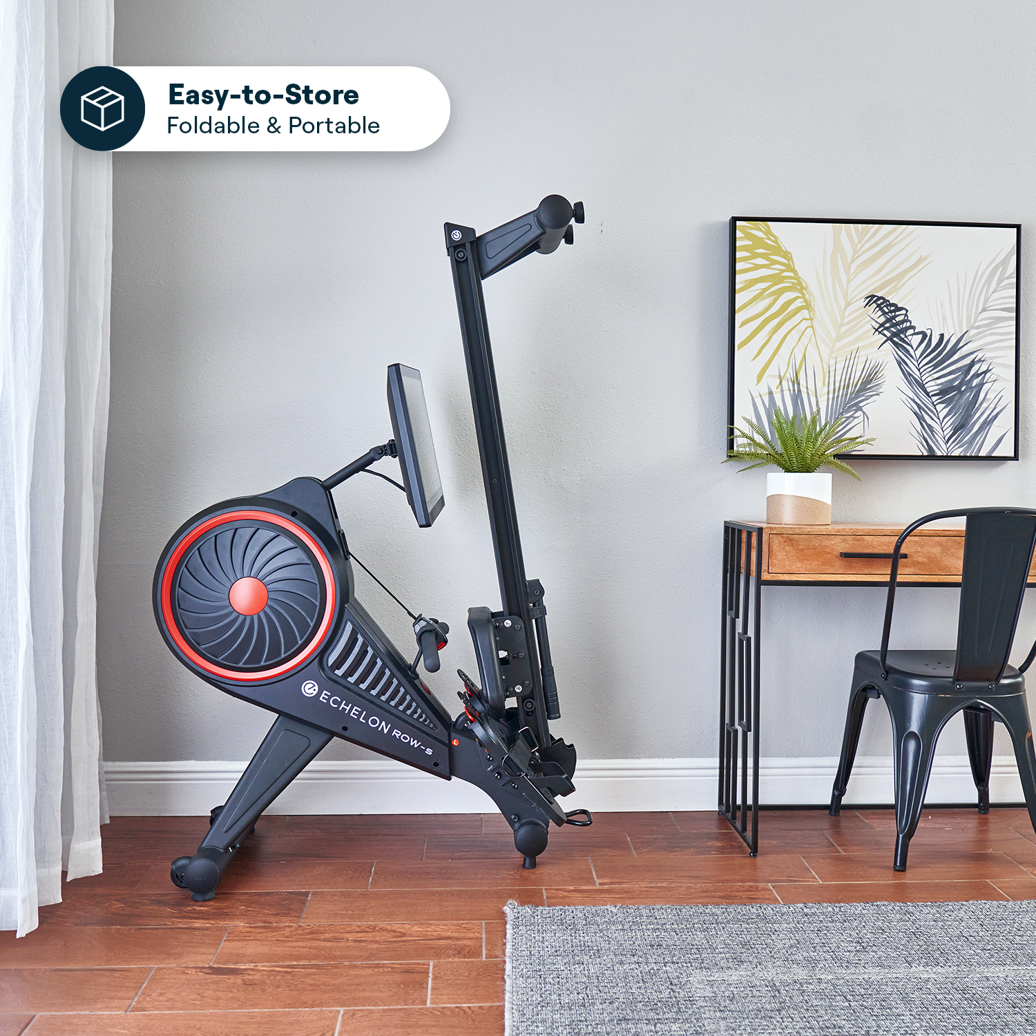 Folded rowing machine beside desk and chair, plant on table.