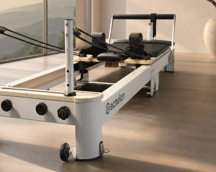 A white Echelon Pilates reformer machine on a wood floor in a room with a large window.