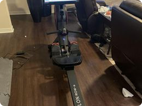 A rowing machine in a living room with a screen and dark wooden floor.