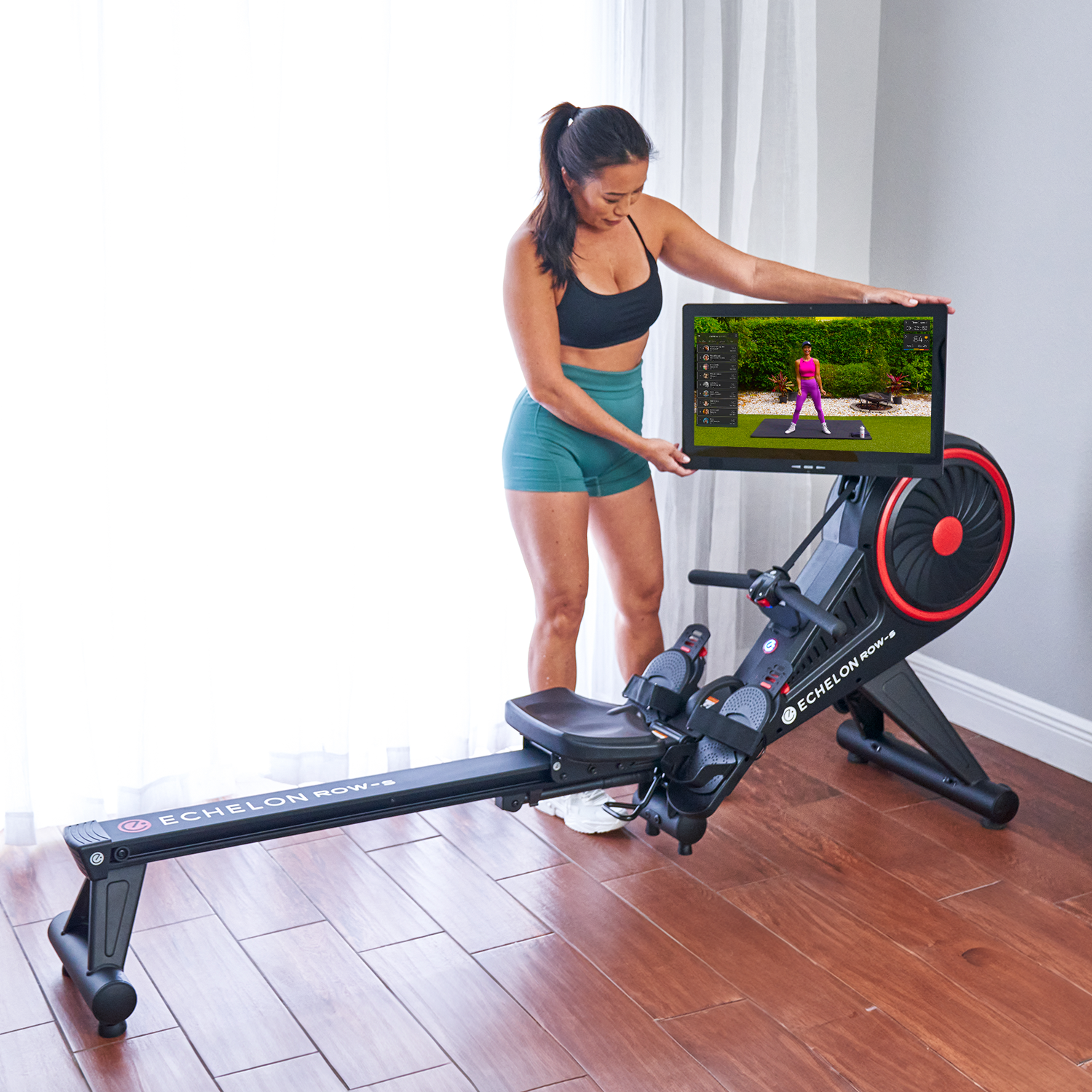 Person adjusting screen on indoor rowing machine with fitness program displayed.