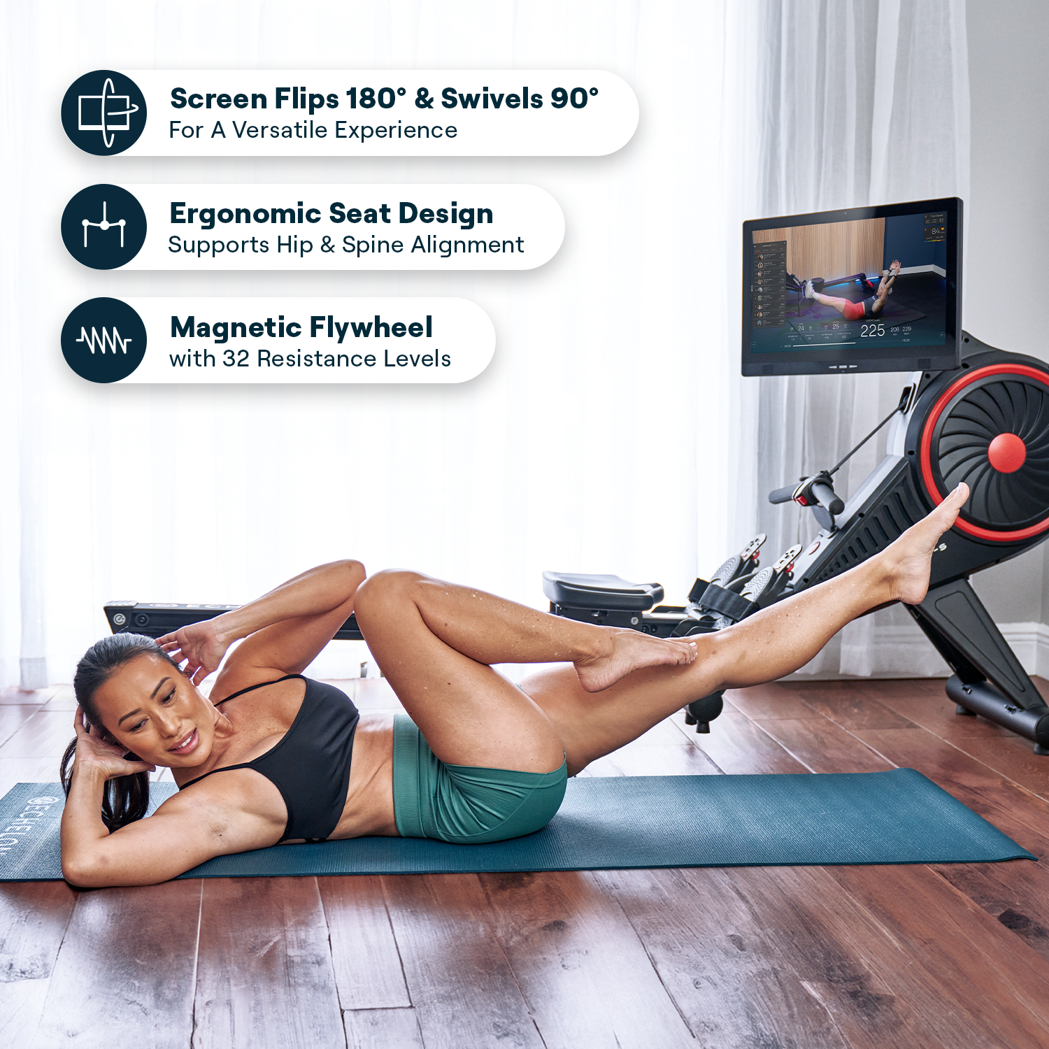 Person exercising on a mat in front of fitness equipment with a screen displaying a workout.