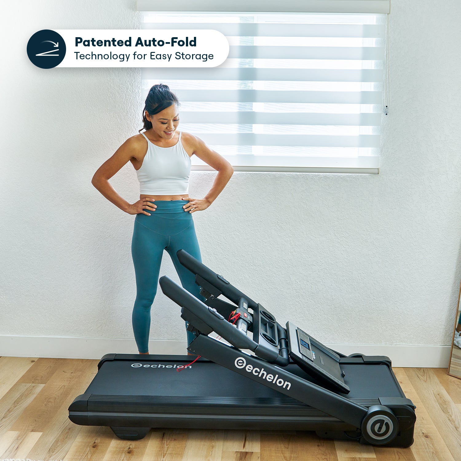 Woman standing next to a folding treadmill in a bright room.
