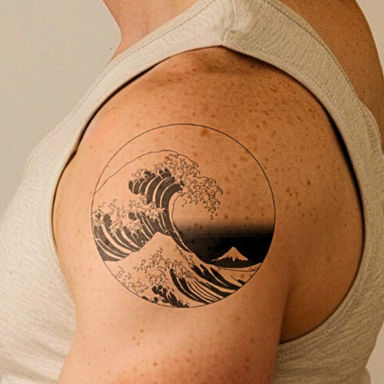 Tattoo of a wave and mountain on a person's upper arm.