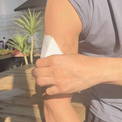 Person applying a white patch to their upper arm outdoors.