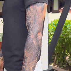 Person with a detailed sleeve tattoo on their arm, standing outdoors.