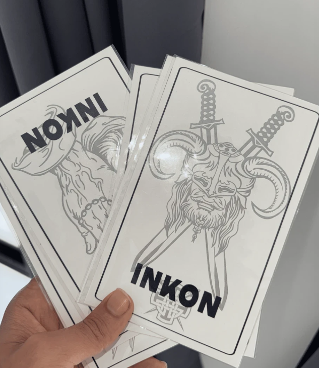 Hand holding illustrated cards with horned skull and swords design.
