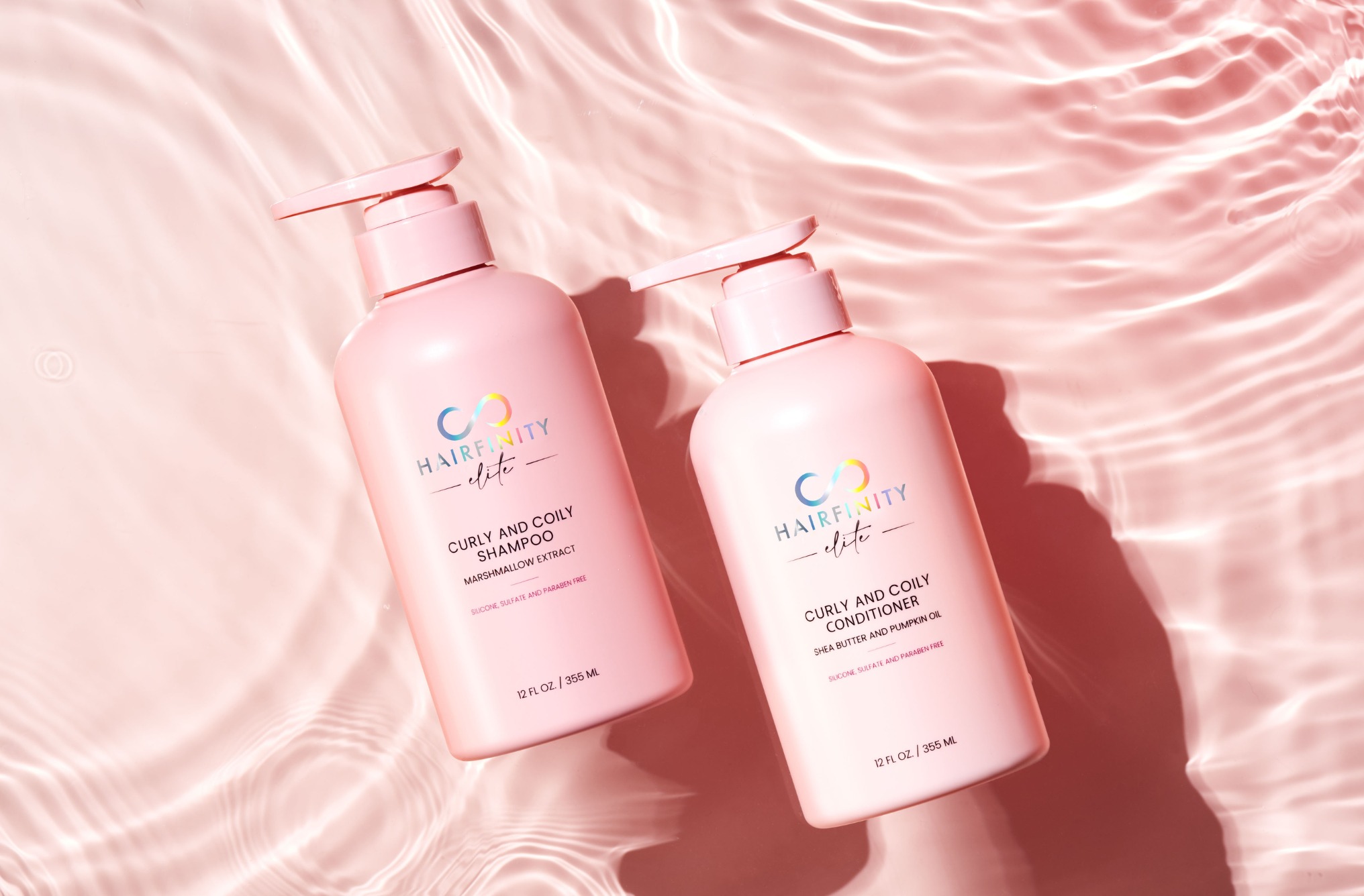 Two pink bottles of hair care products on a textured pink background.