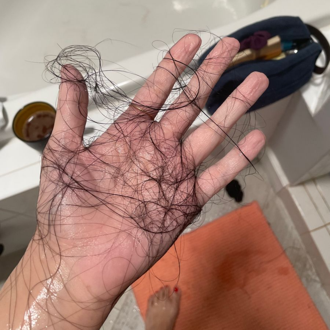 A hand holding a clump of wet hair over an orange bath mat.