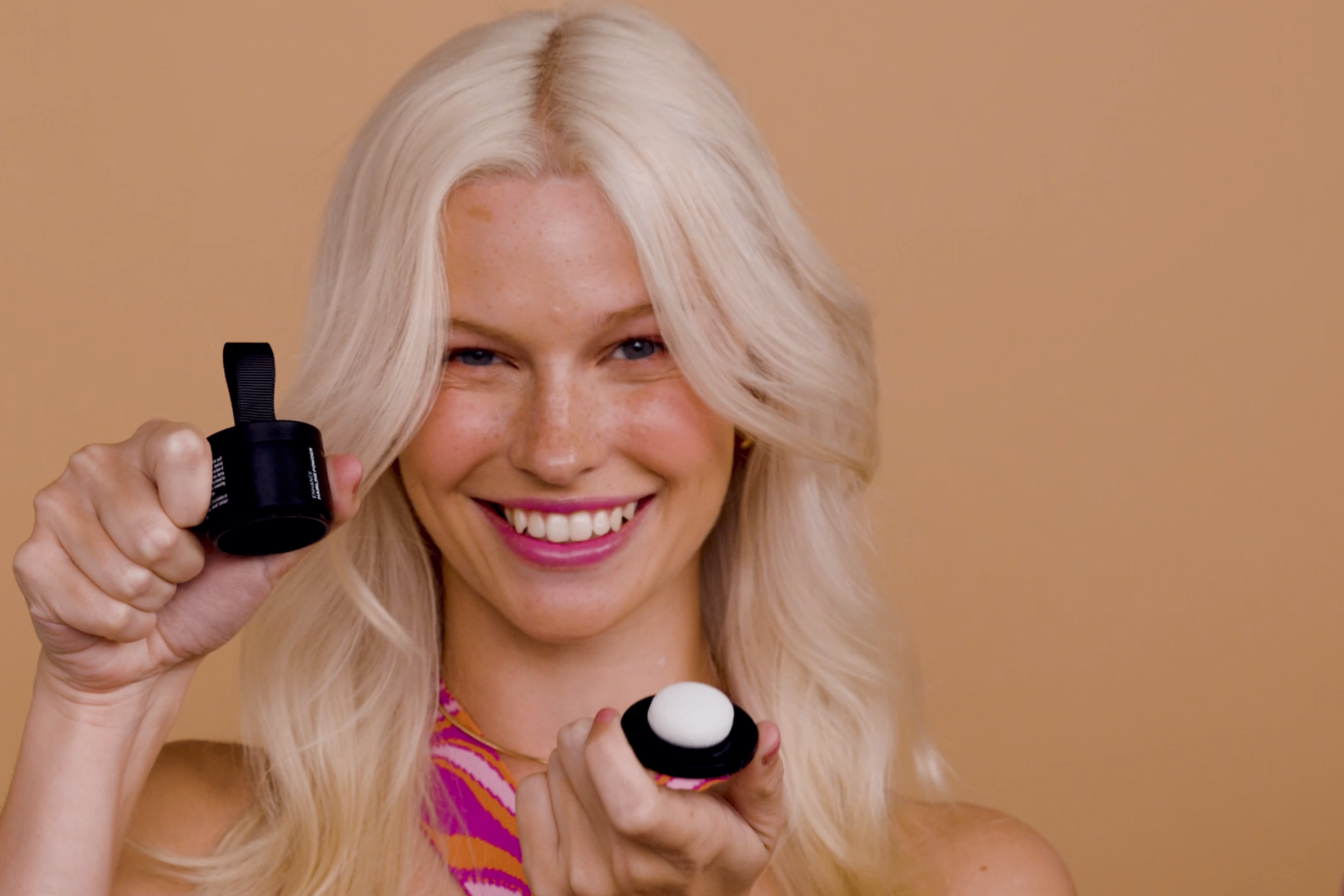 Smiling person holding two small round containers against a peach background.
