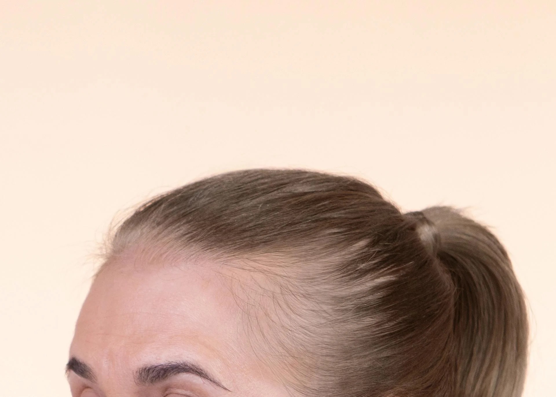 Close-up of a person's hair in a ponytail on a neutral background.