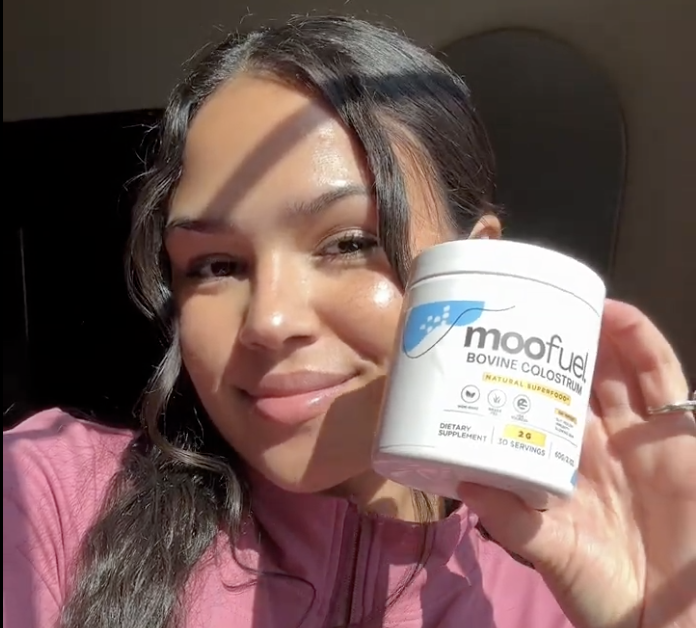 Person holding a container of Moofuel Bovine Colostrum, smiling in sunlight.