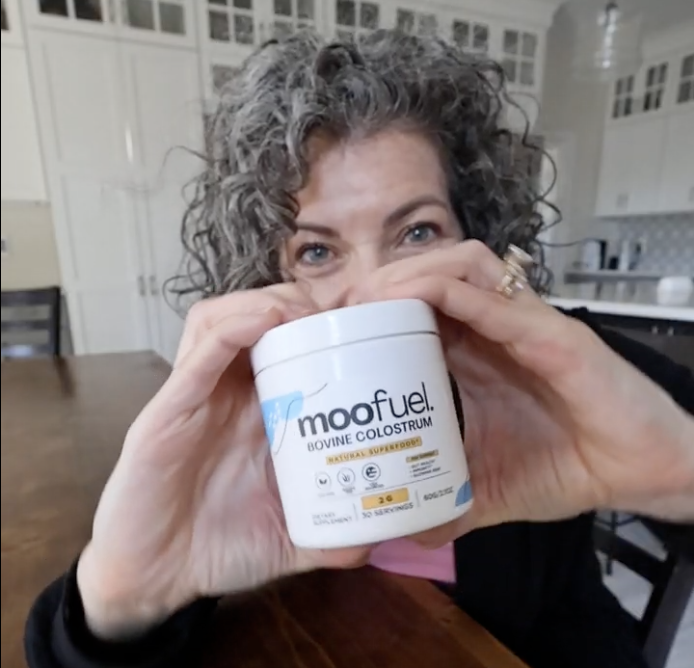 Person holding a container of Moofuel Bovine Colostrum in a kitchen.