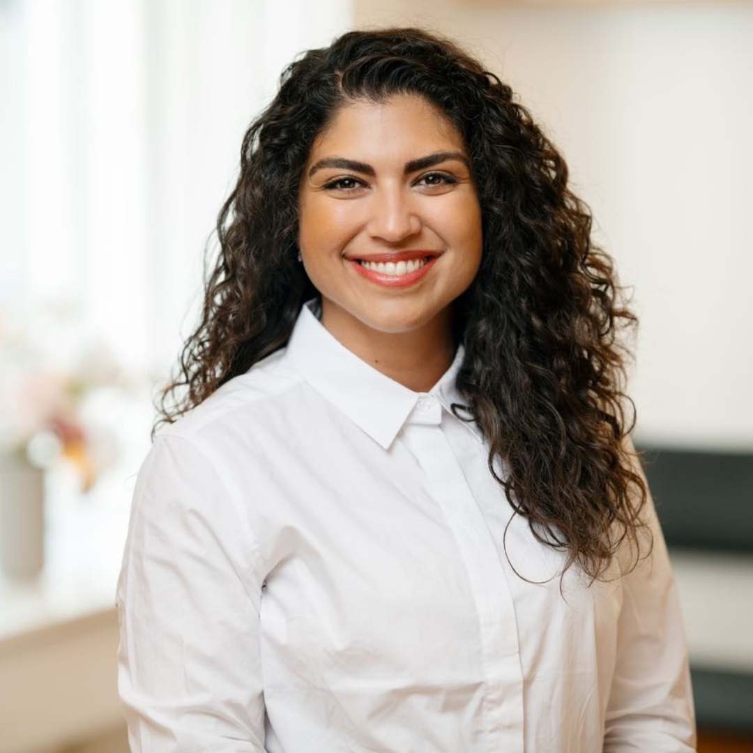 Person with curly hair smiling, wearing a white shirt.