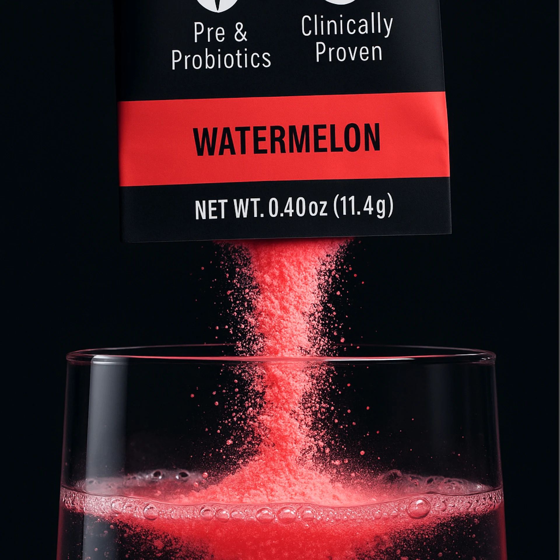 Red watermelon-flavored pre and probiotic powder being poured from a packet into a glass of water.