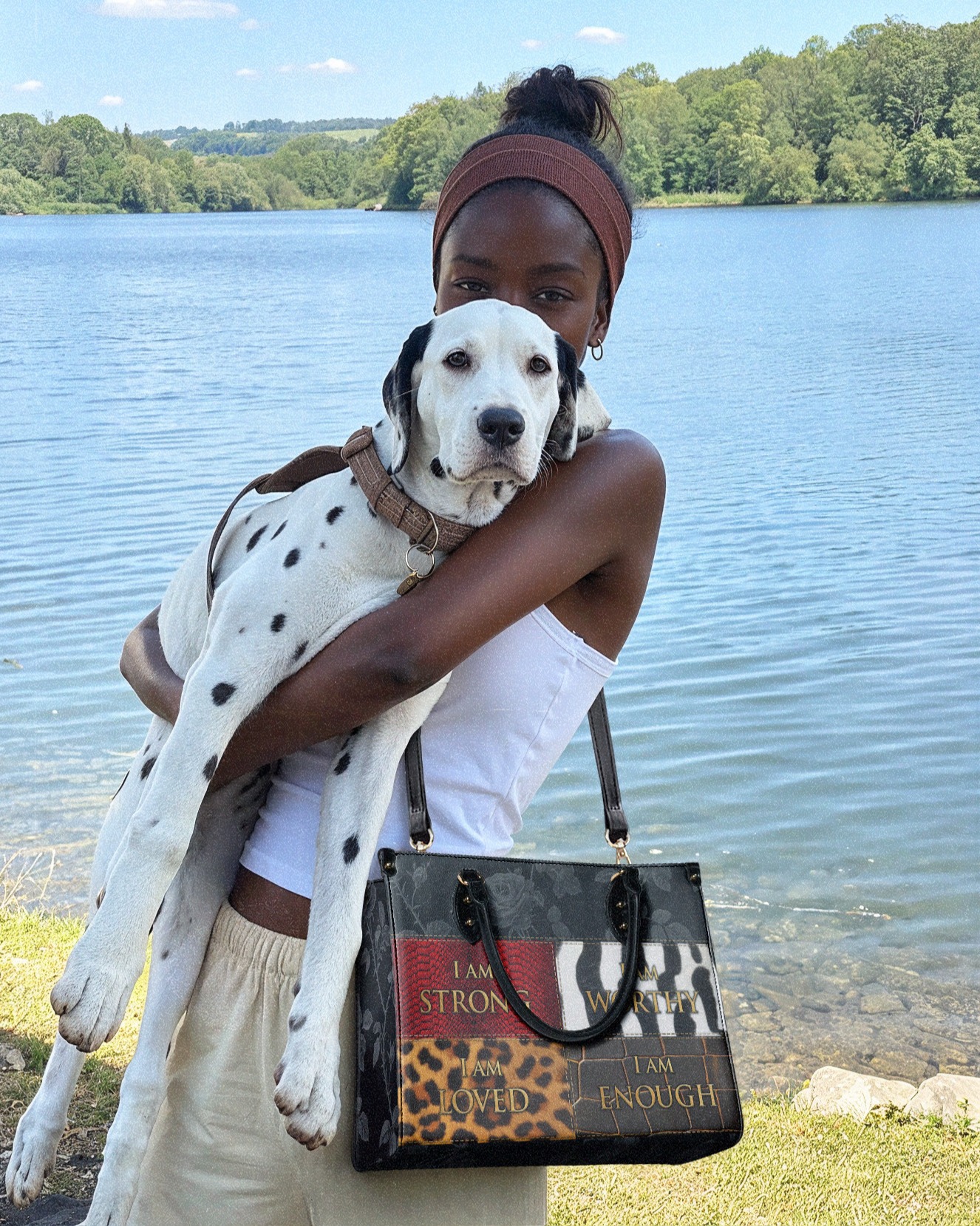Person holding a Dalmatian puppy by a lake, with trees in the background.