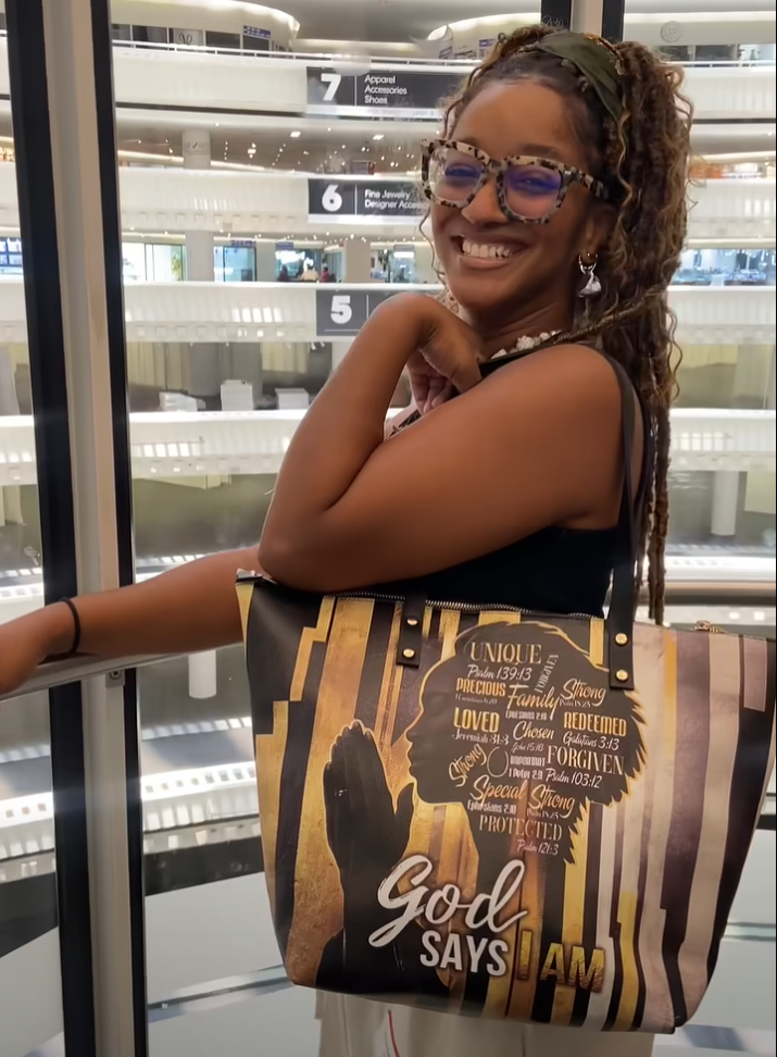 Smiling person with glasses holding a decorative bag, standing in front of elevator doors.