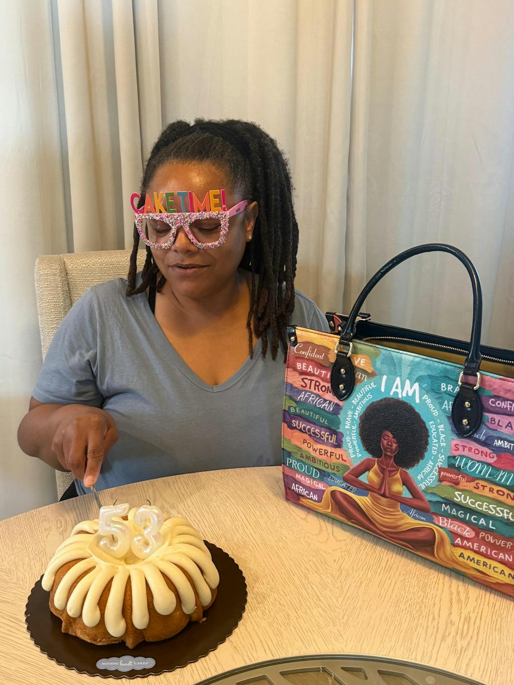 Person wearing 'CAKE TIME!' glasses with a cake and artistic bag on the table.