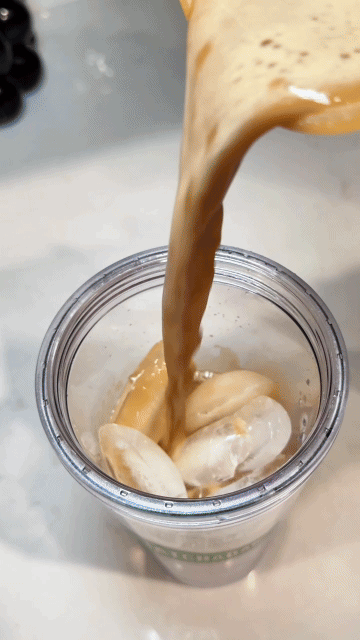 Coffee being poured over ice in a clear cup.