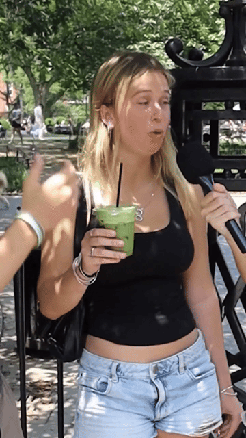 Person holding a green drink, speaking into a microphone outdoors.