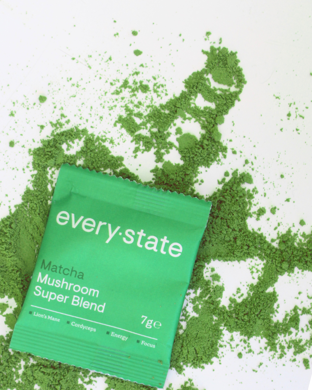 Green packet of matcha mushroom blend on spilled powder.