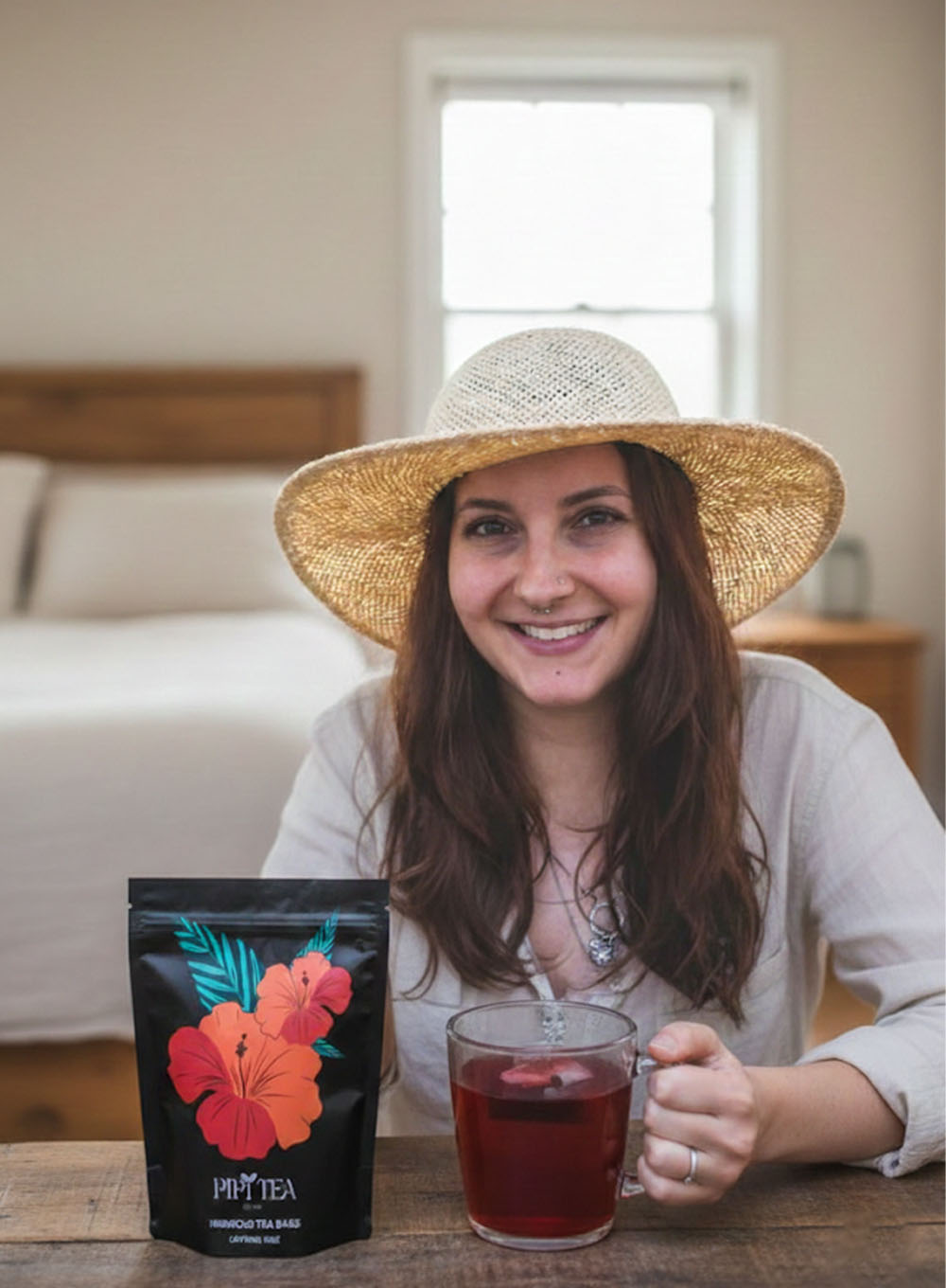 A smiling woman in a straw hat holds a mug of red tea next to a pouch of Pipi Tea.