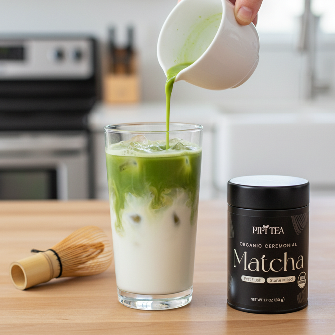A person pours green matcha tea into a glass of iced milk, next to a whisk and container.
