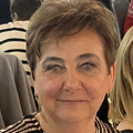A person smiling in an indoor setting with blurred background.