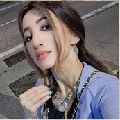 Person taking a selfie outdoors, wearing a blue jacket and necklace.