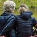 Two people sitting outdoors, viewed from behind, with greenery in the background.
