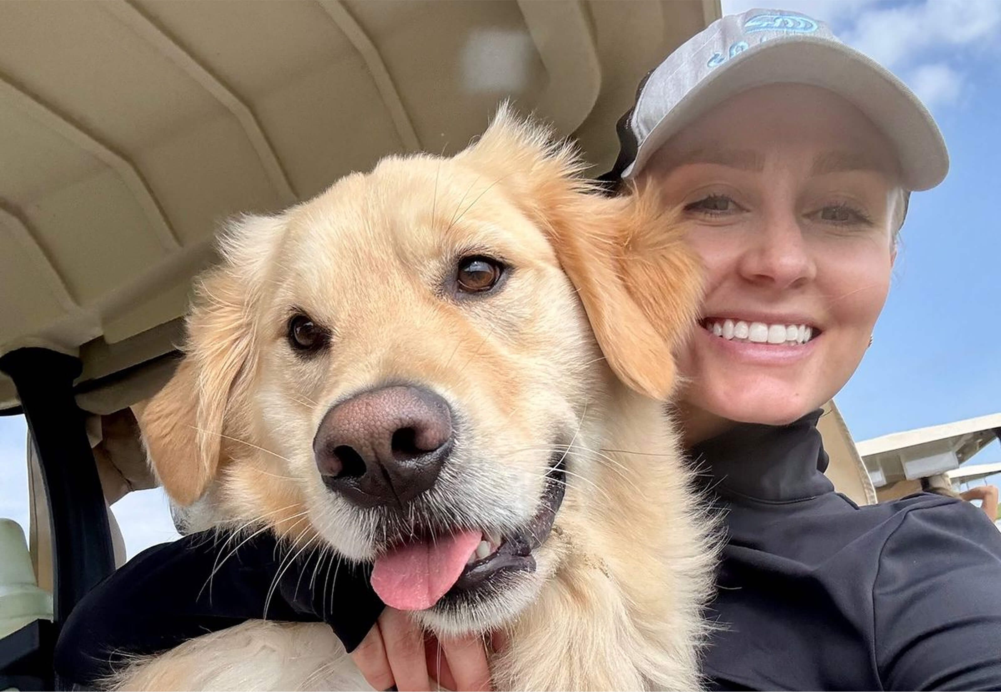 Smiling person with a golden retriever in a golf cart.