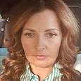 A close-up photo of a woman with styled, reddish-brown hair, wearing a striped collared shirt.