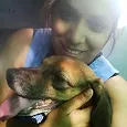 A person with a bright smile holds a brown dog with floppy ears close to their face.