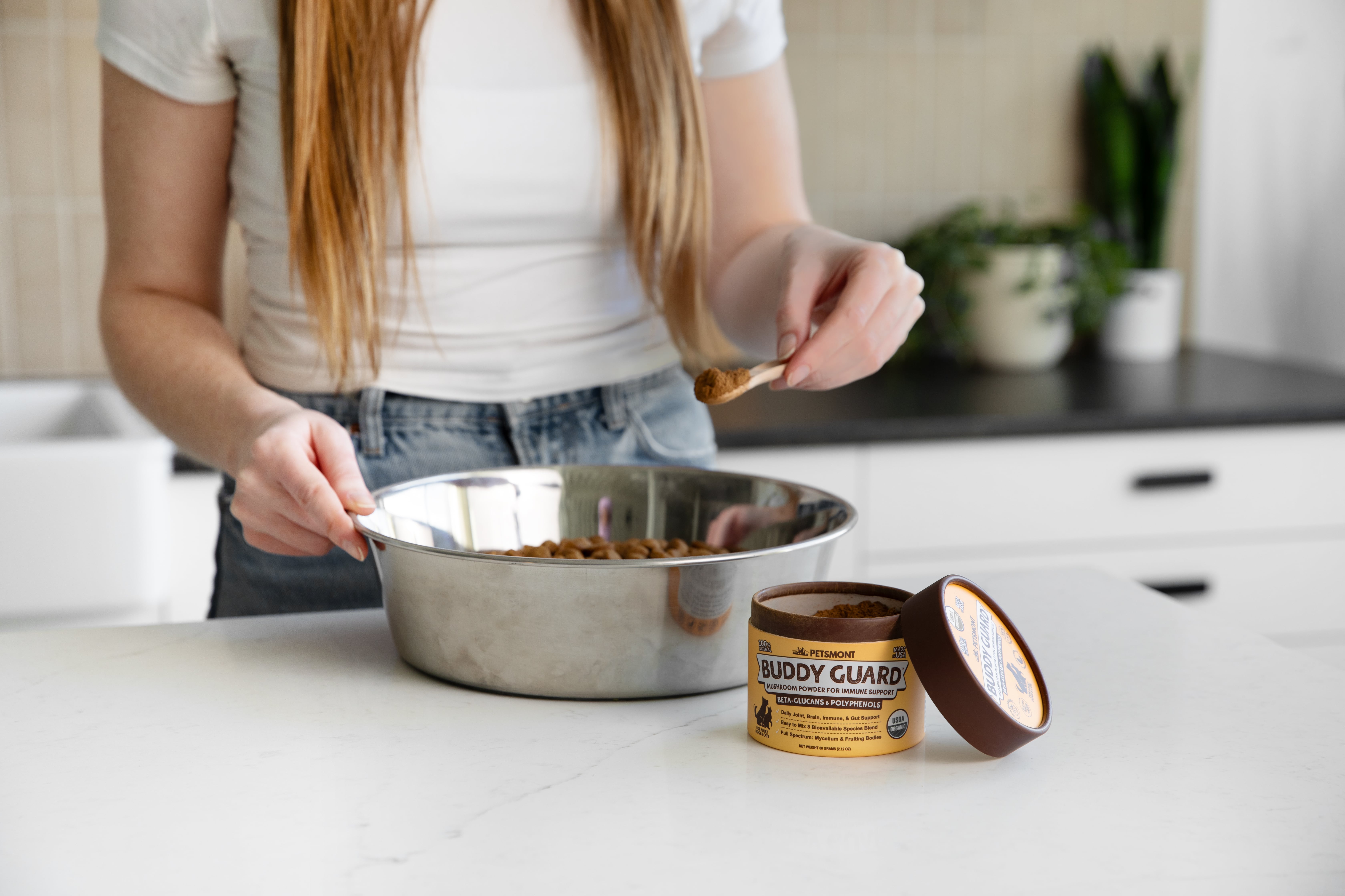 Person adding powder to pet food bowl in kitchen.