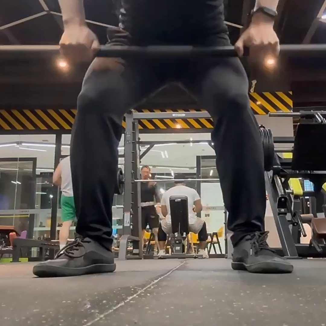 Person lifting a barbell in a gym with others in the background.
