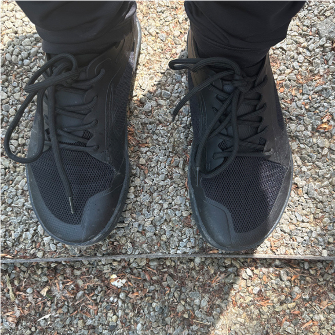 Person wearing black sneakers standing on gravel.