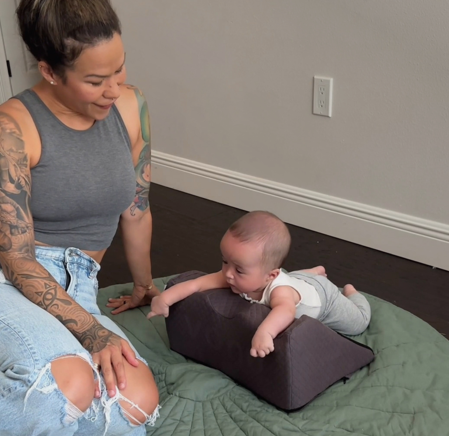 Woman sitting on floor next to baby on cushion, both on a green mat.