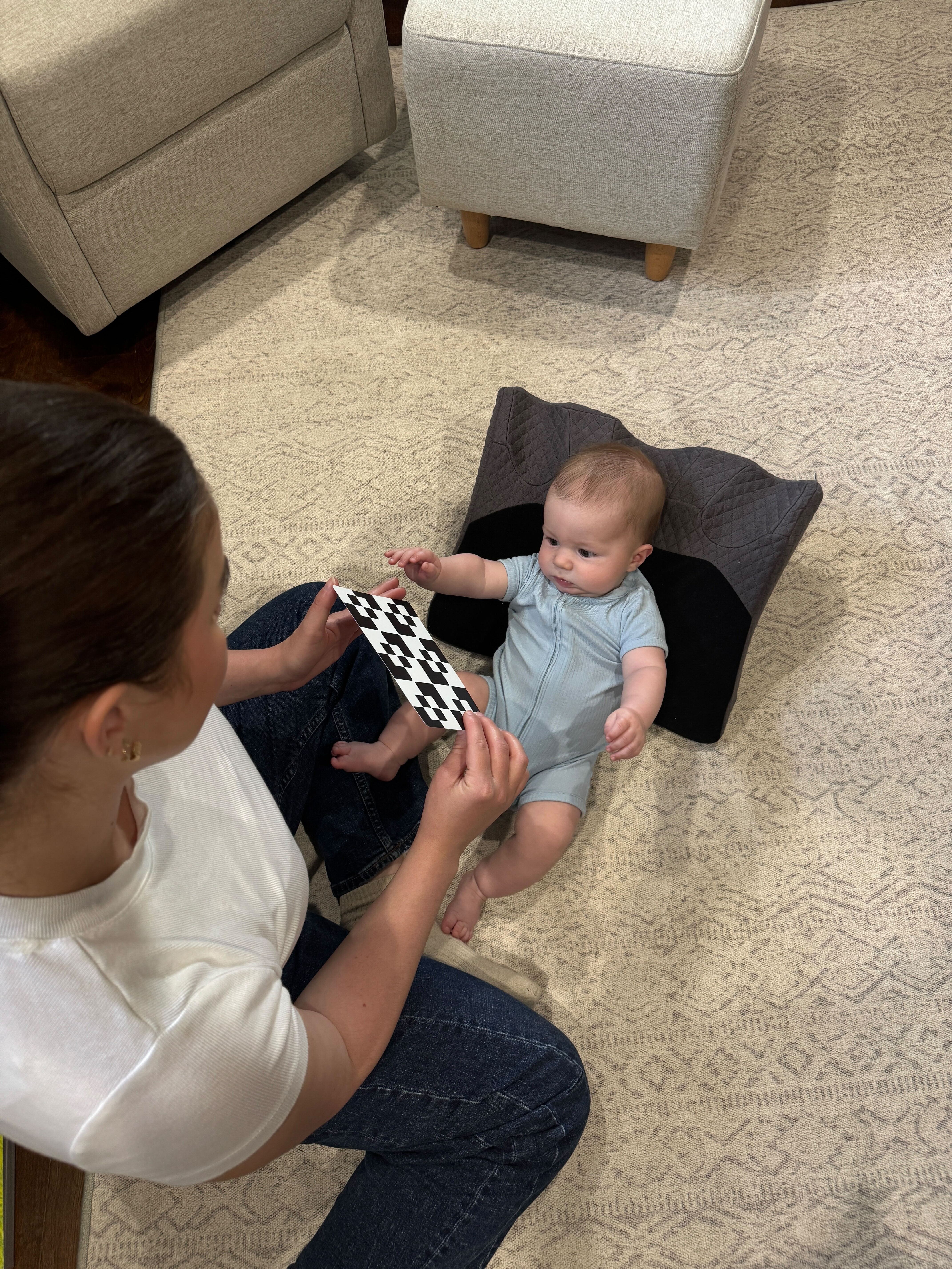 Woman showing a black and white card to a baby on a cushion.