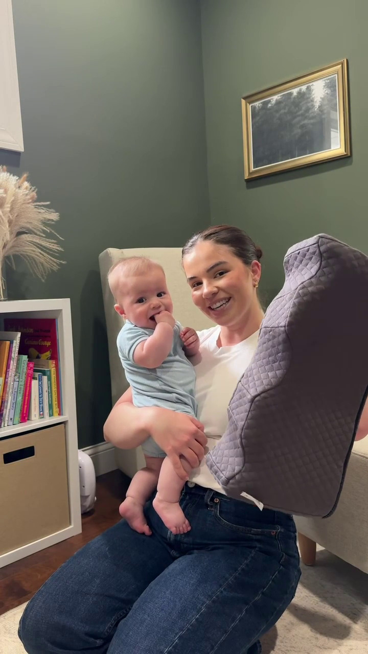 Woman holding a baby in a cozy room with books and decor.