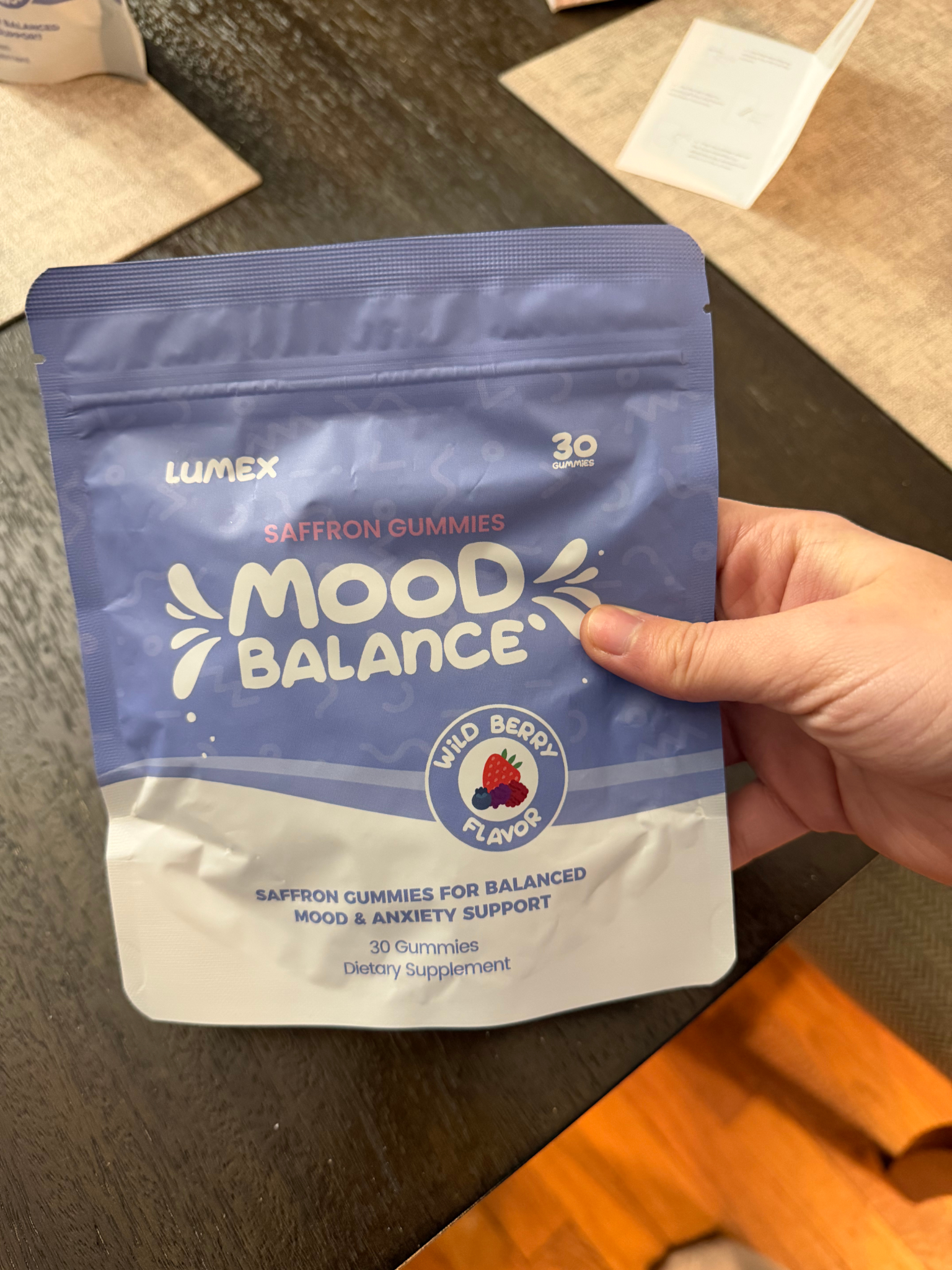 A hand holds a purple and white pouch of Lumex Saffron Gummies Mood Balance dietary supplement.