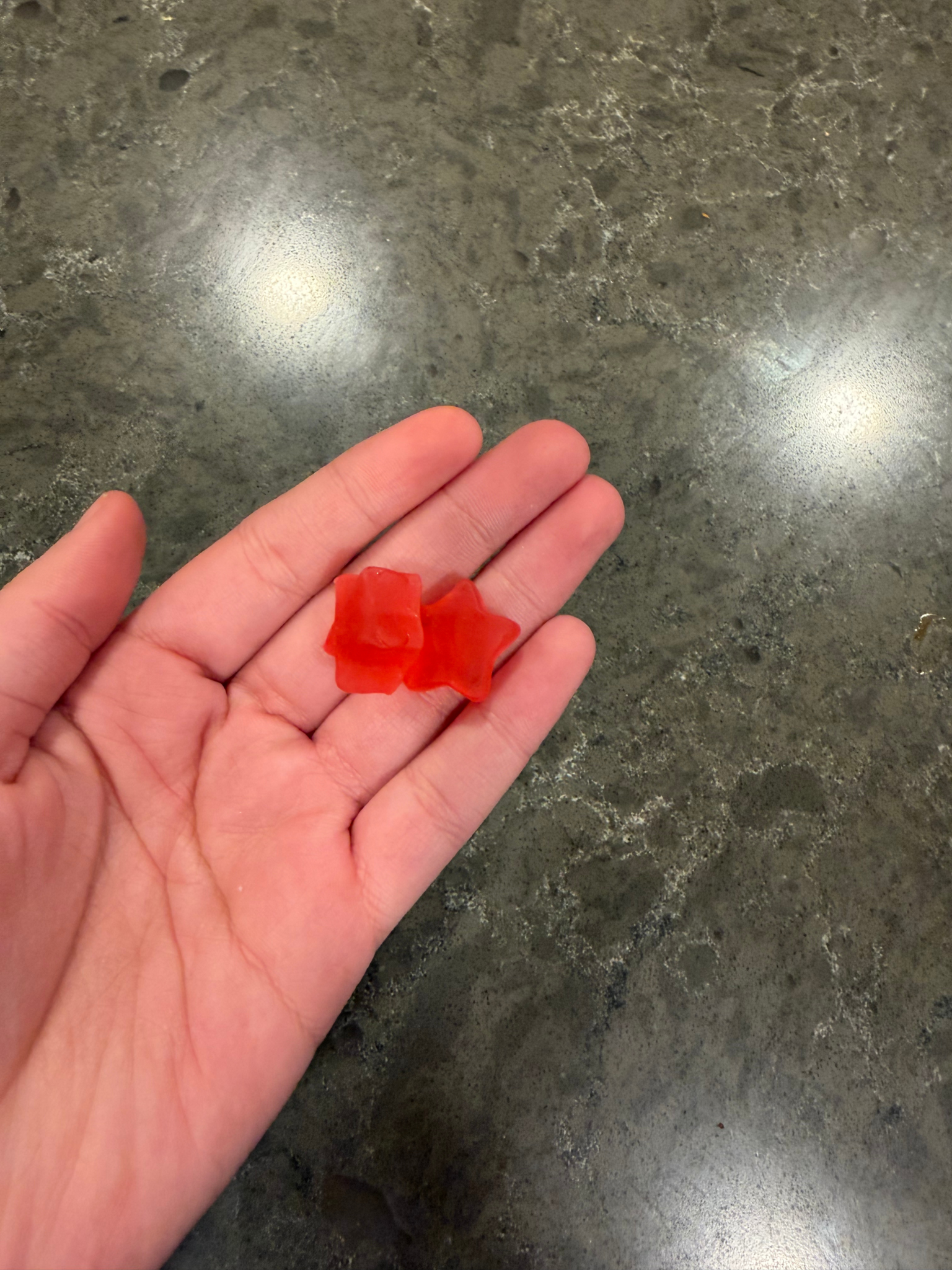 A person's open hand holding two red star-shaped gummy candies over a dark countertop.
