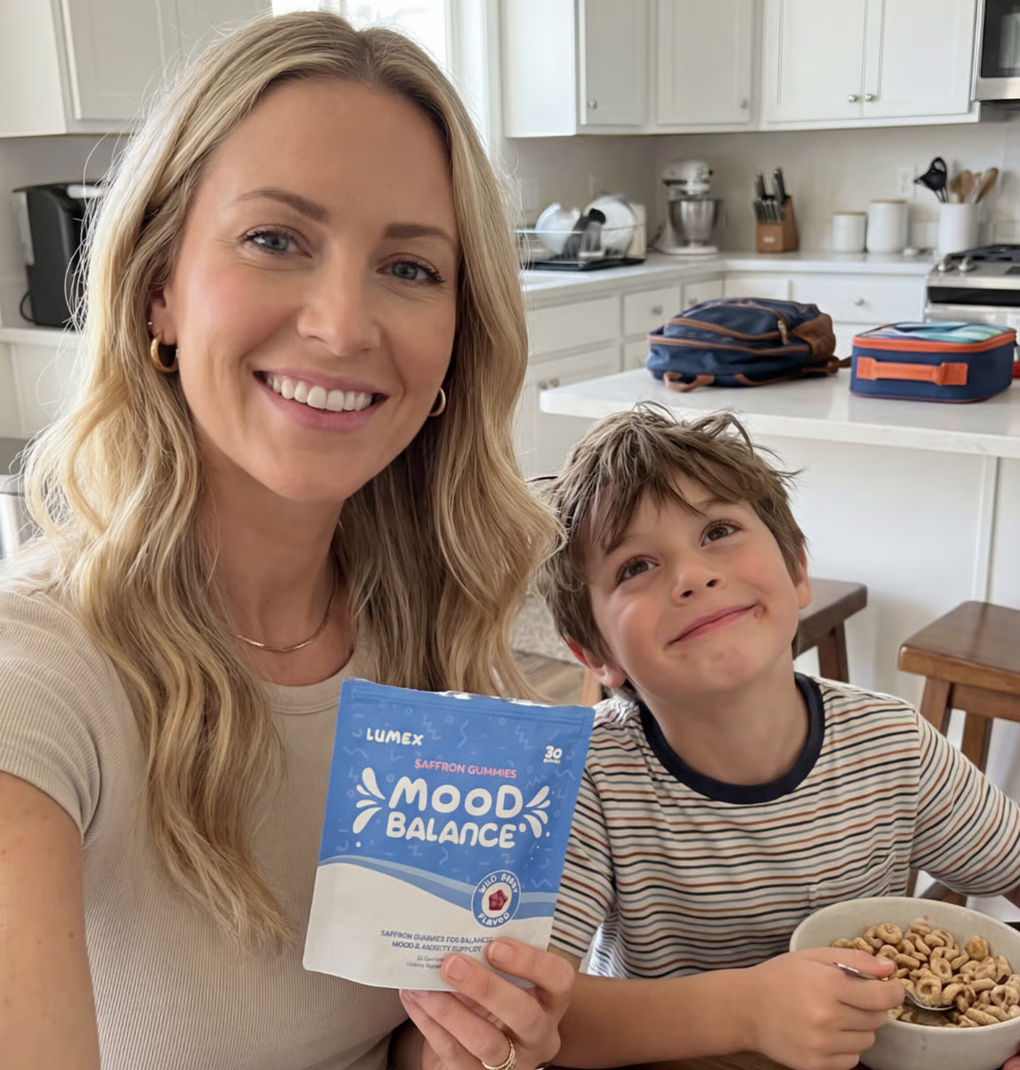 A smiling woman holds a pouch of Lumex Mood Balance gummies next to a young boy eating cereal.