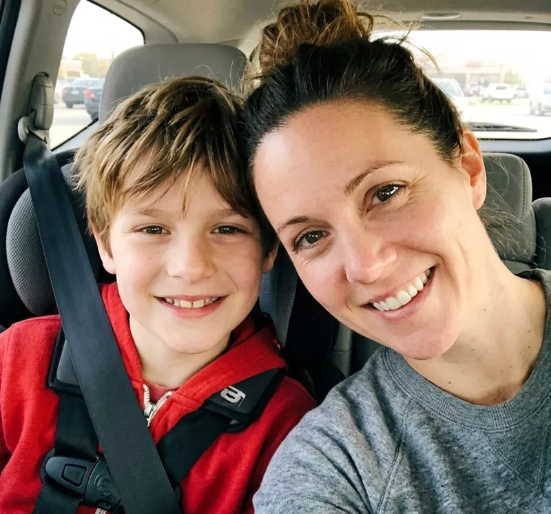 A woman and a young boy smiling for a selfie in a car.