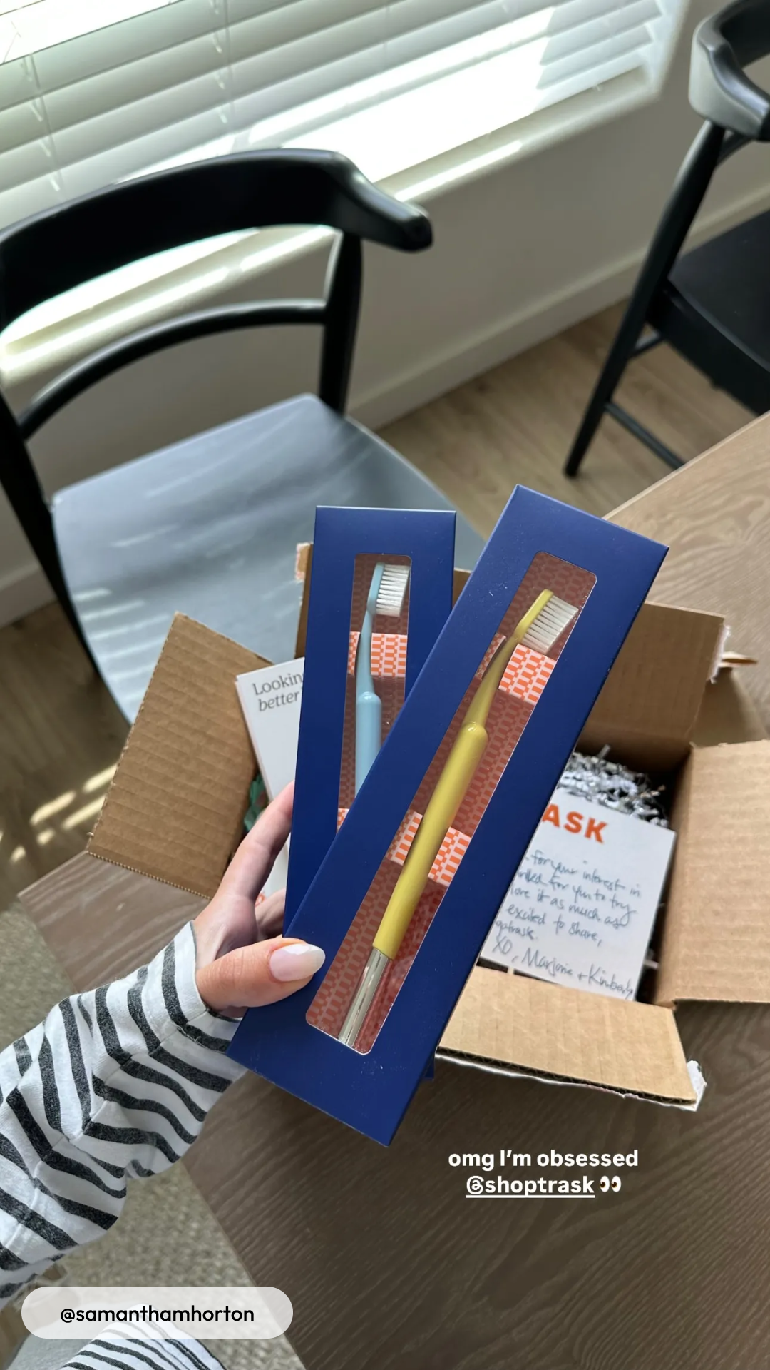 Person holding two boxed toothbrushes over an open cardboard box.