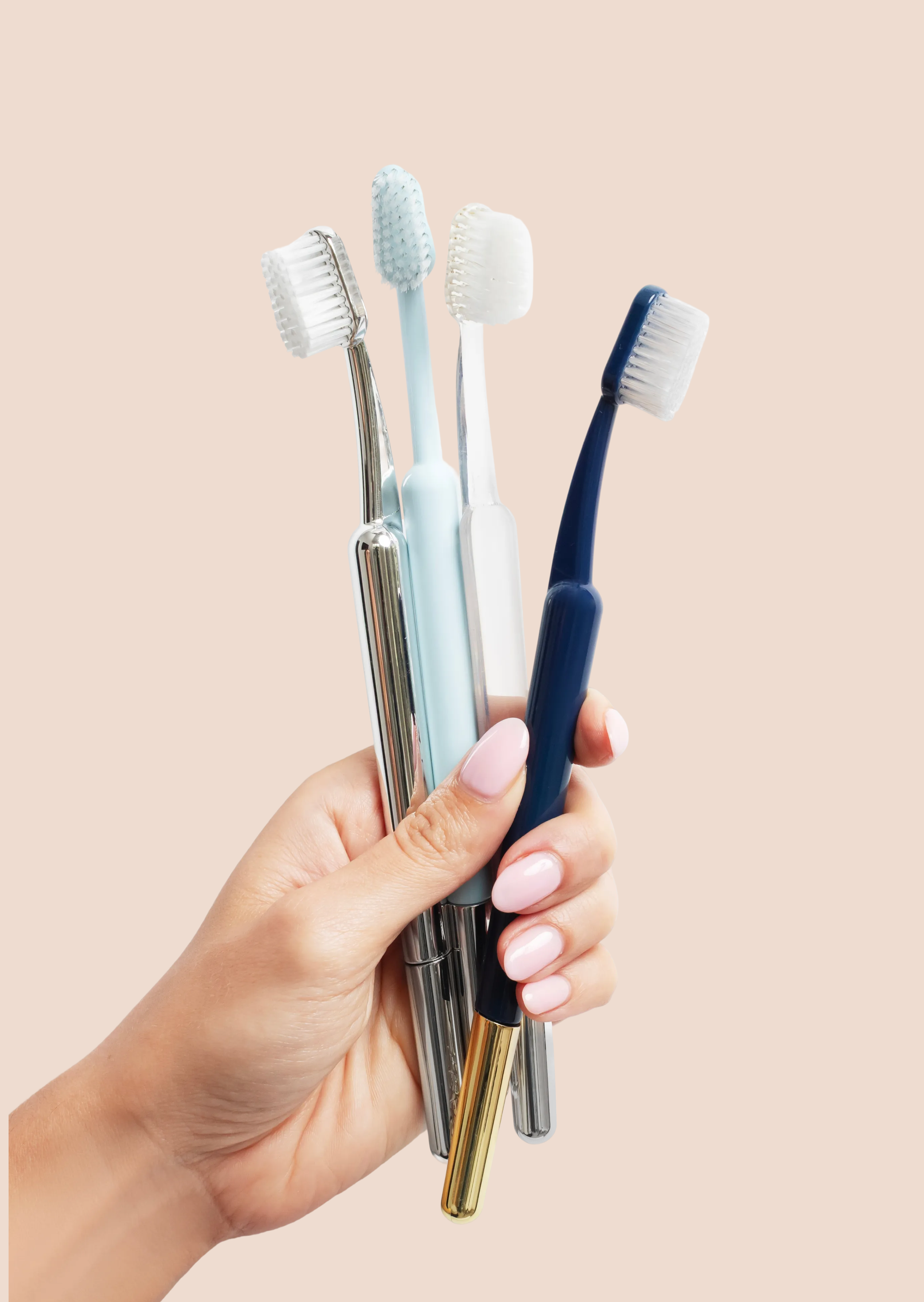 Hand holding four toothbrushes against a beige background.