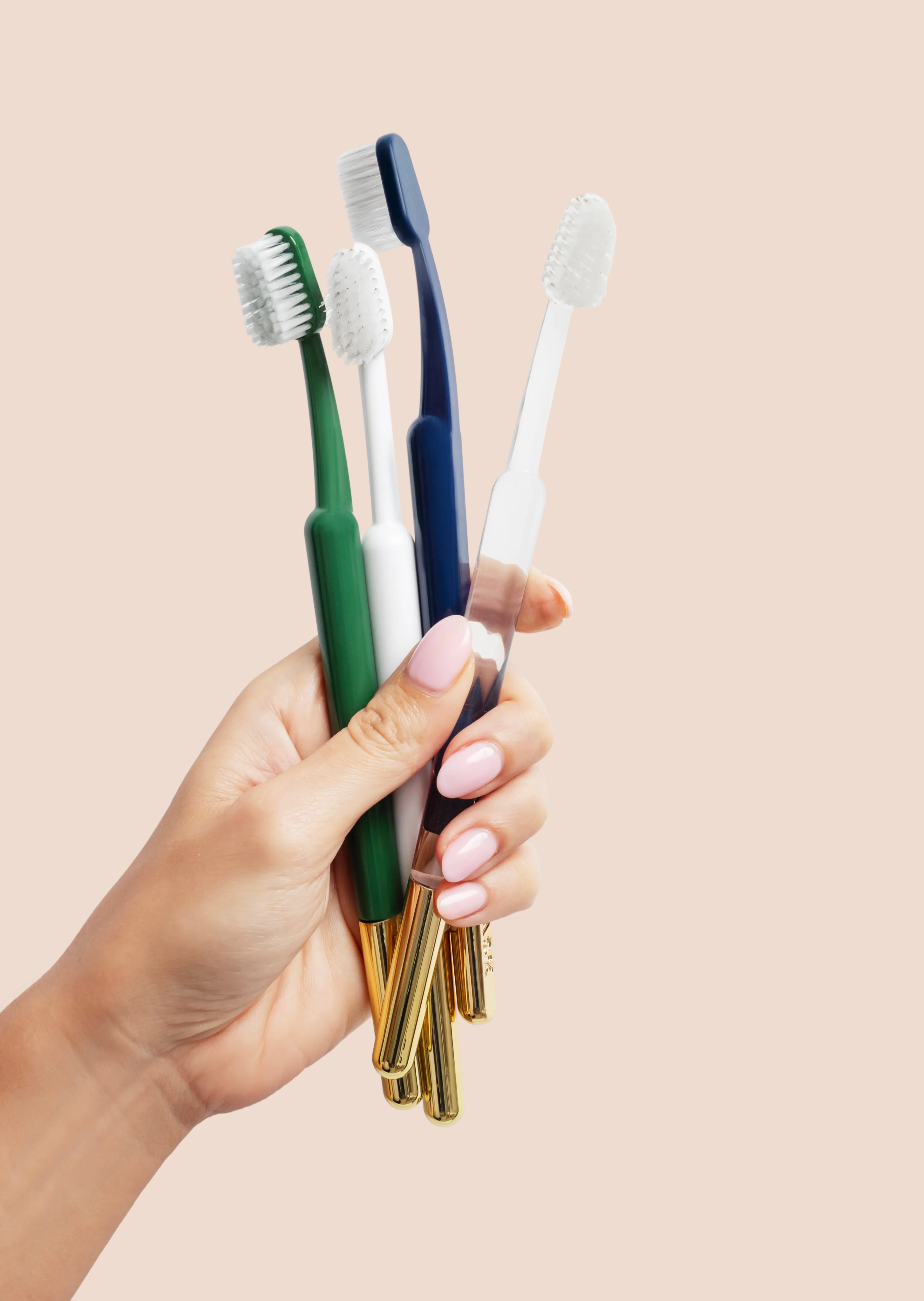 Hand holding four colorful toothbrushes with gold handles.
